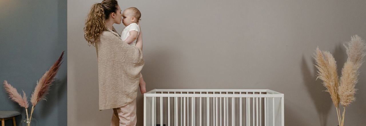 Mother standing near crib and cuddling her baby