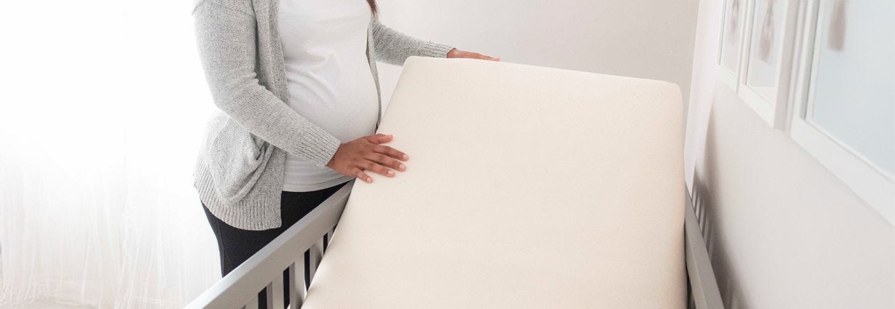 pregnant person fitting a naturepedic mattress in a crib