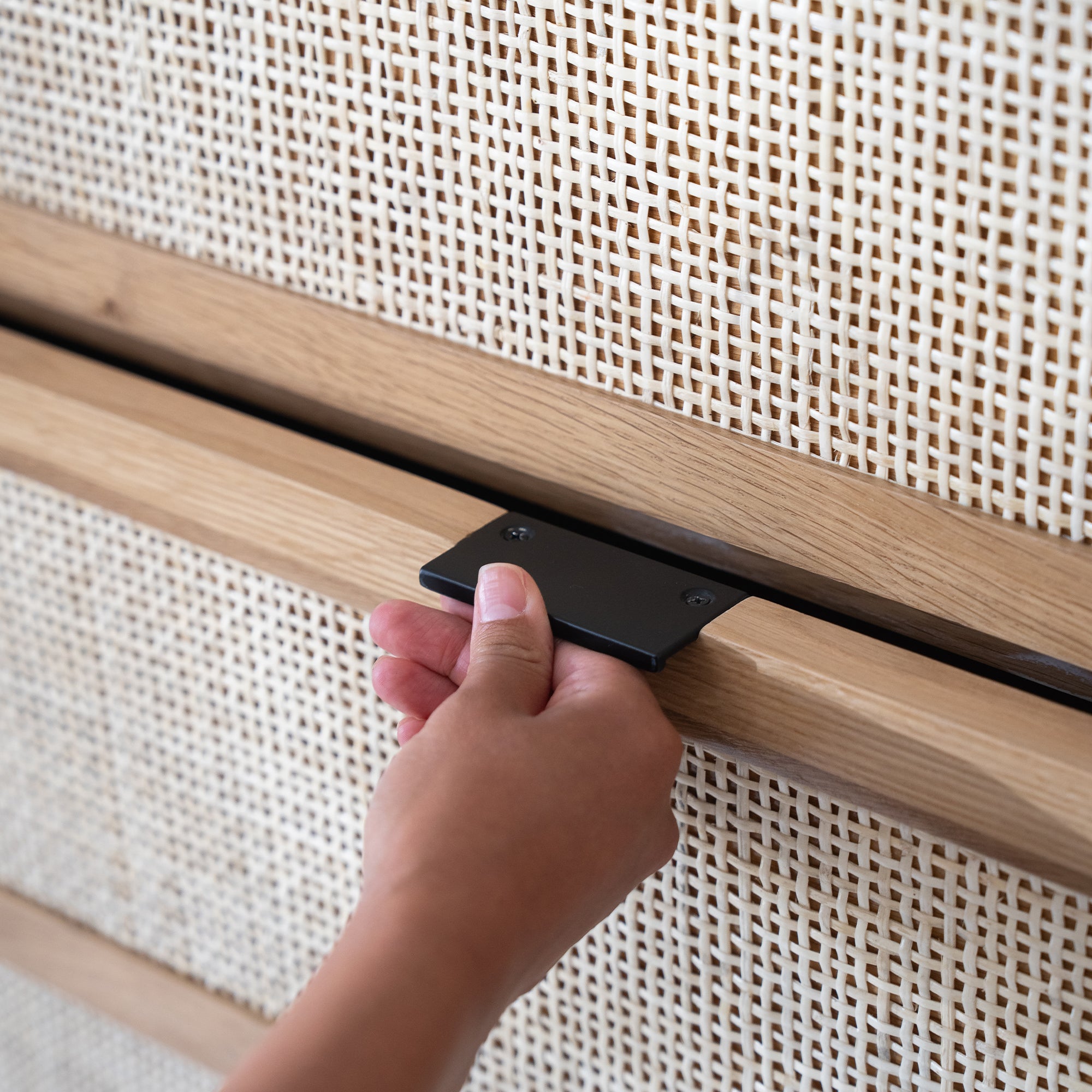 A close-up of a hand opening a woven wood drawer with a black pull.