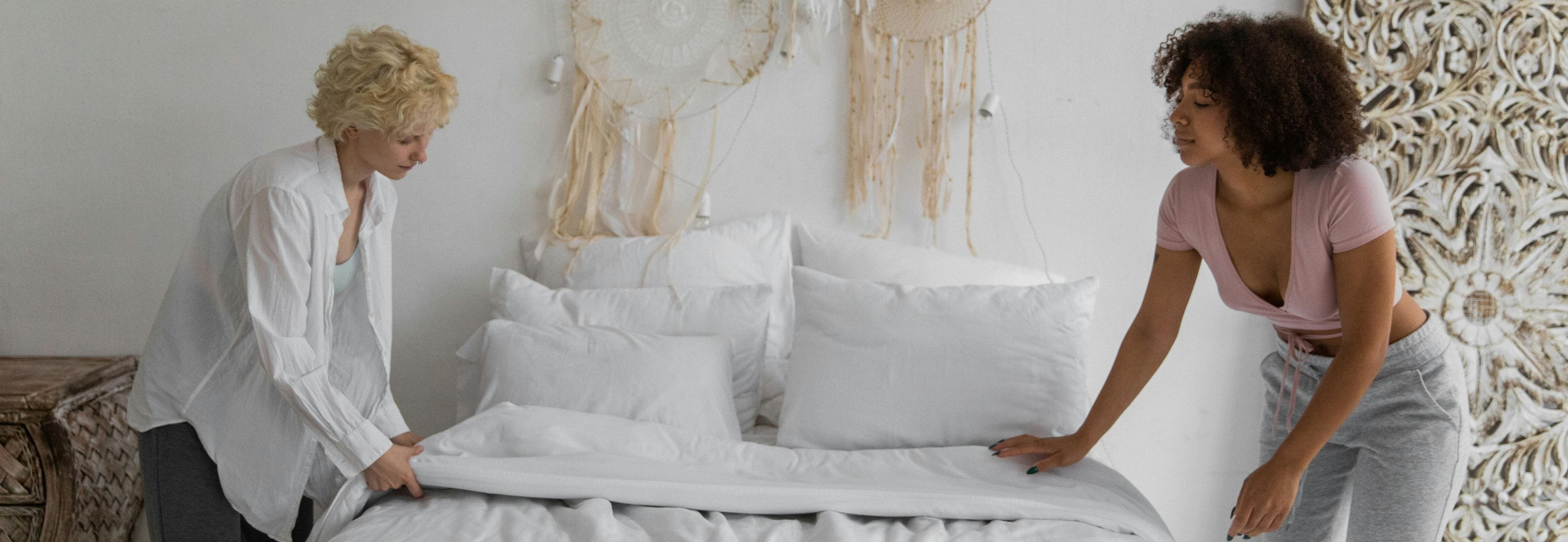 two women putting sheets on a bed