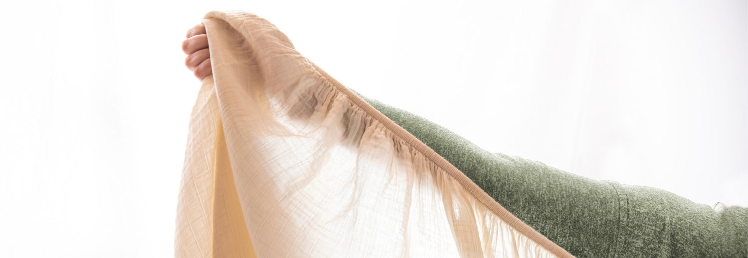 person holding cotton muslin baby crib sheet up to the light
