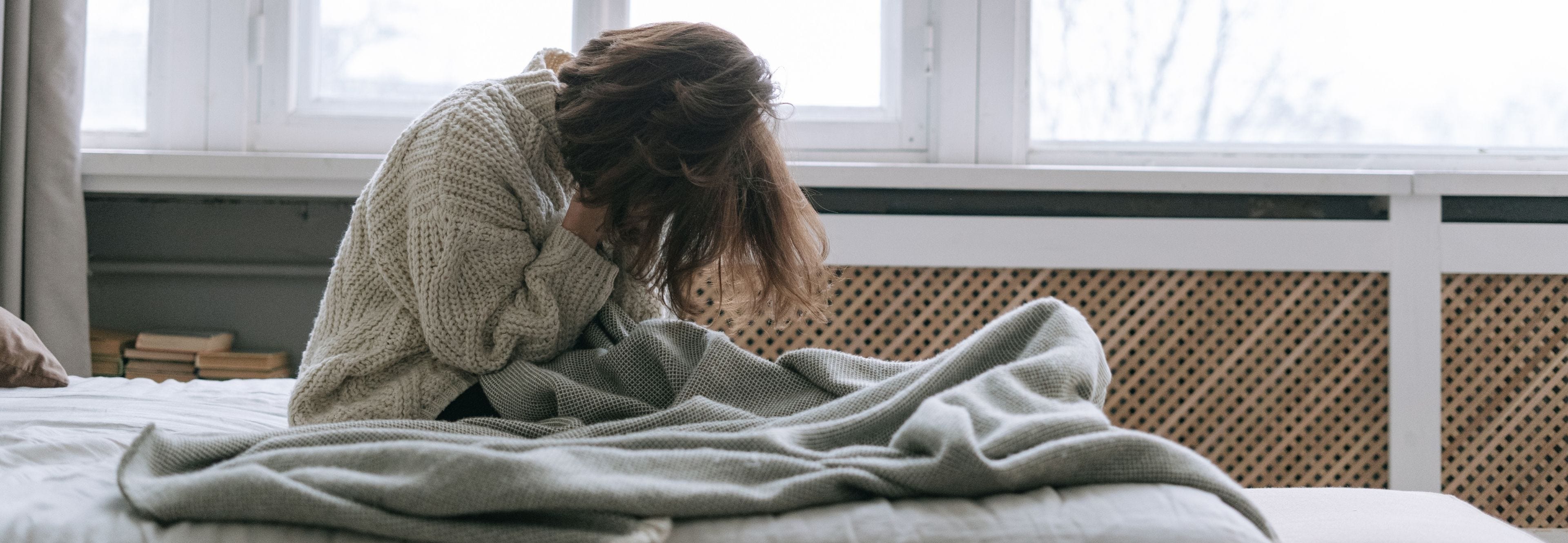 Woman sitting up in bed during the day with head in hands