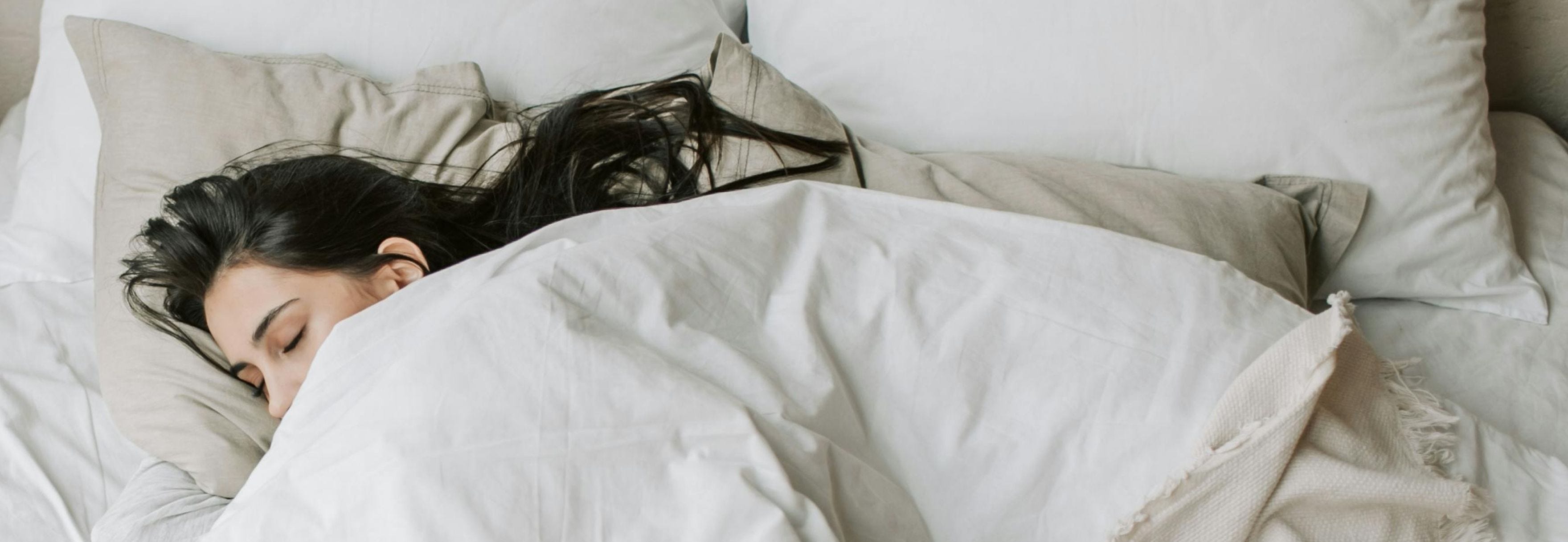 Wide view of a person sleeping alone in a neatly made bed with neutral bedding and pillows