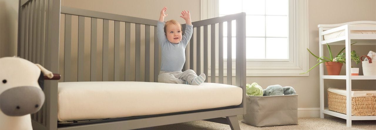 Baby sitting up on their crib and lifting their arms