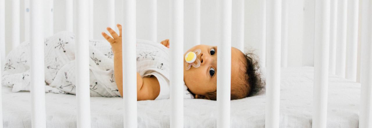 Baby with pacifier lying on back and looking through the crib slats