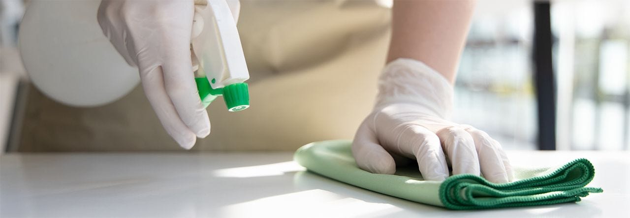 Someone's hand, in rubber gloves, spraying a cleaning solution that off-gasses VOCs