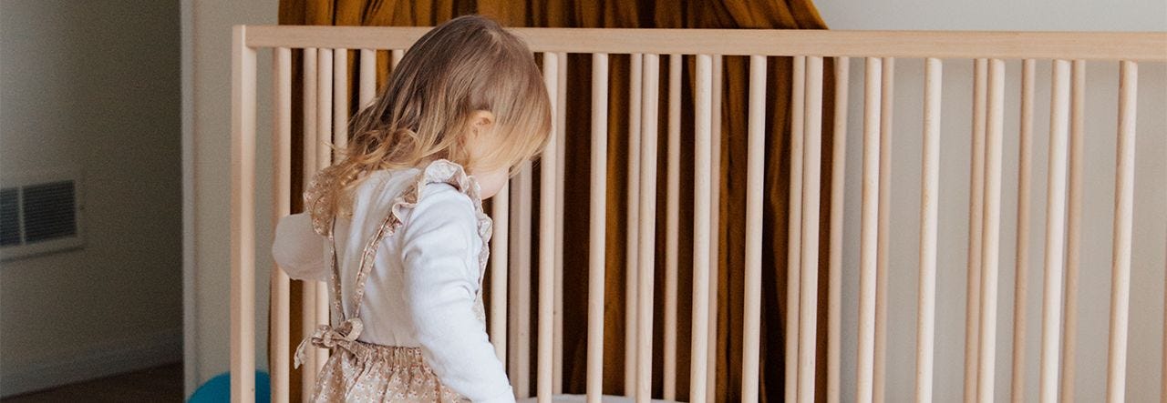 Toddler girl standing near her crib in a beautiful organic nursery
