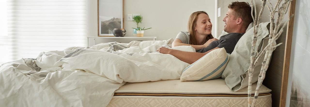 Couple cuddling in bed on their Naturepedic mattress