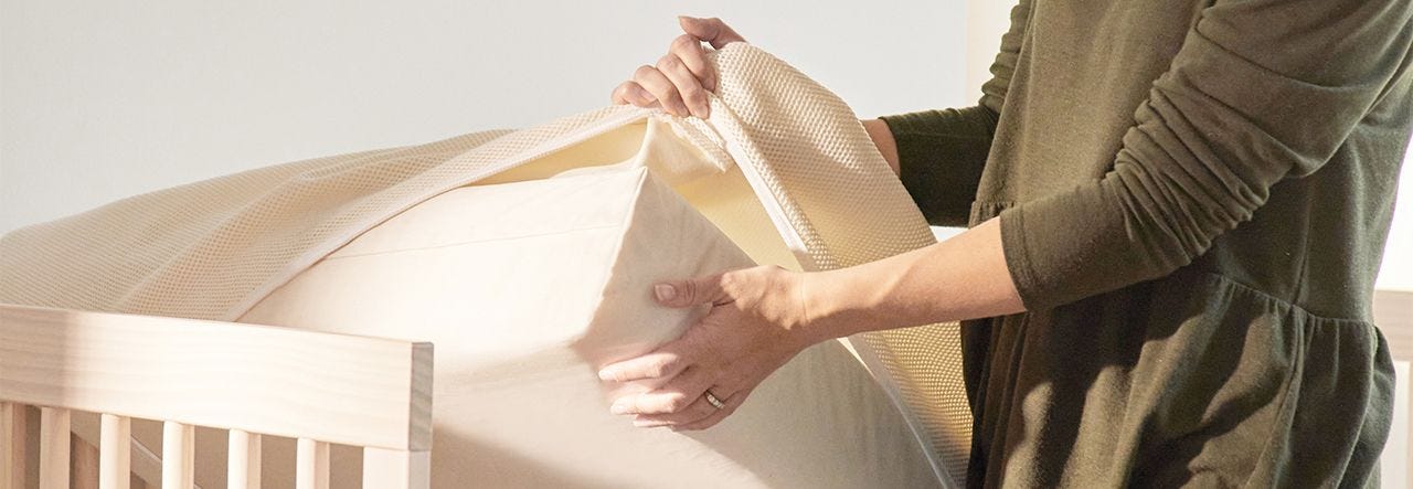 Mom removing a waterproof protector pad from a crib mattress