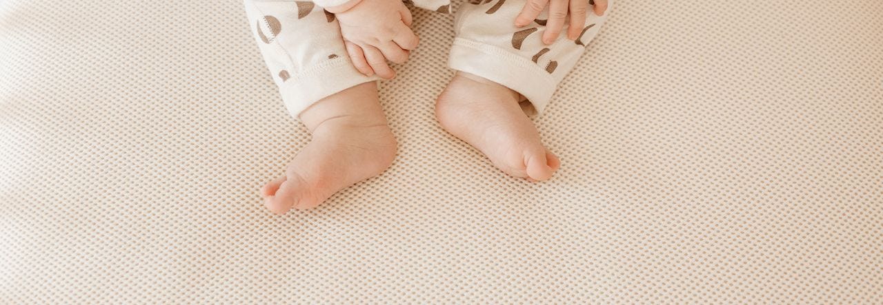 Image of Naturepedic breathable crib mattress with baby feet and hands at the top of the image