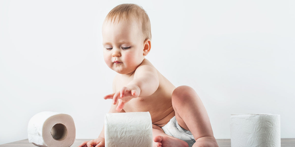 Potty training baby reaching for rolls of toilet paper