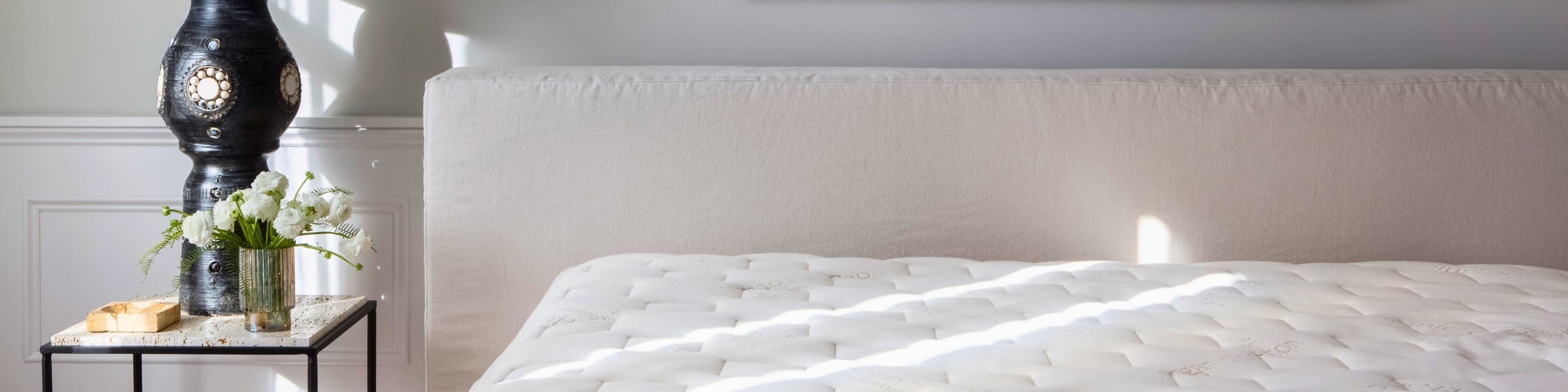White mattress on a bed with a nightstand and decorative items in a bedroom setting.