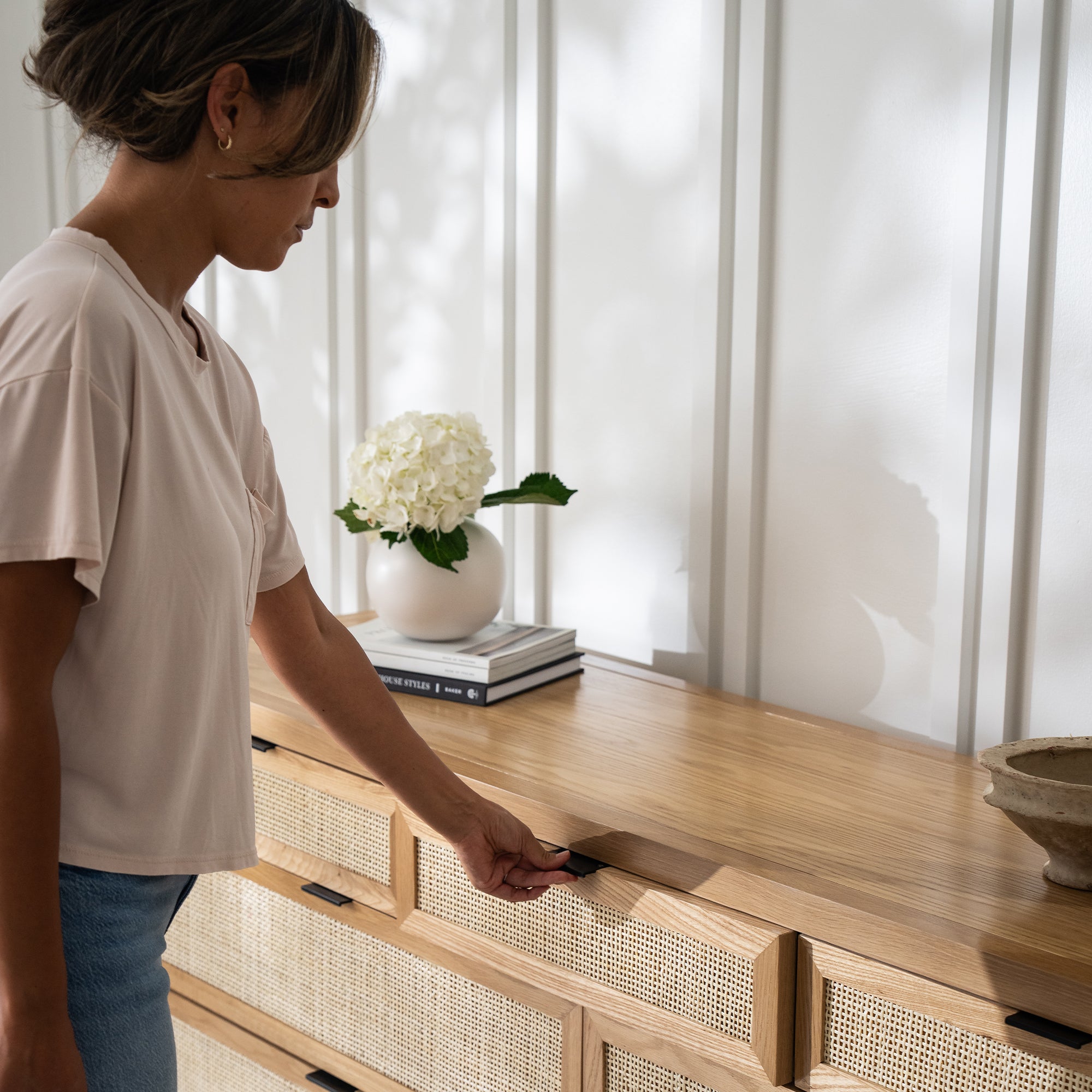 Woman opening the top drawer of the Arienzo dresser with rattan-front drawers.