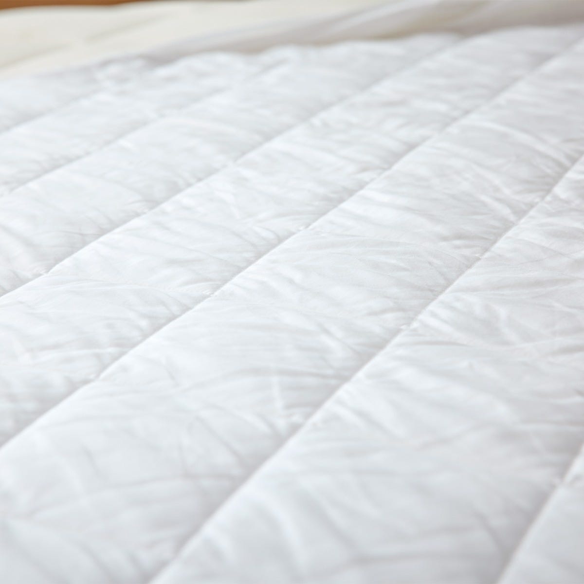 Close-up of a white quilted mattress protector pad on a bed