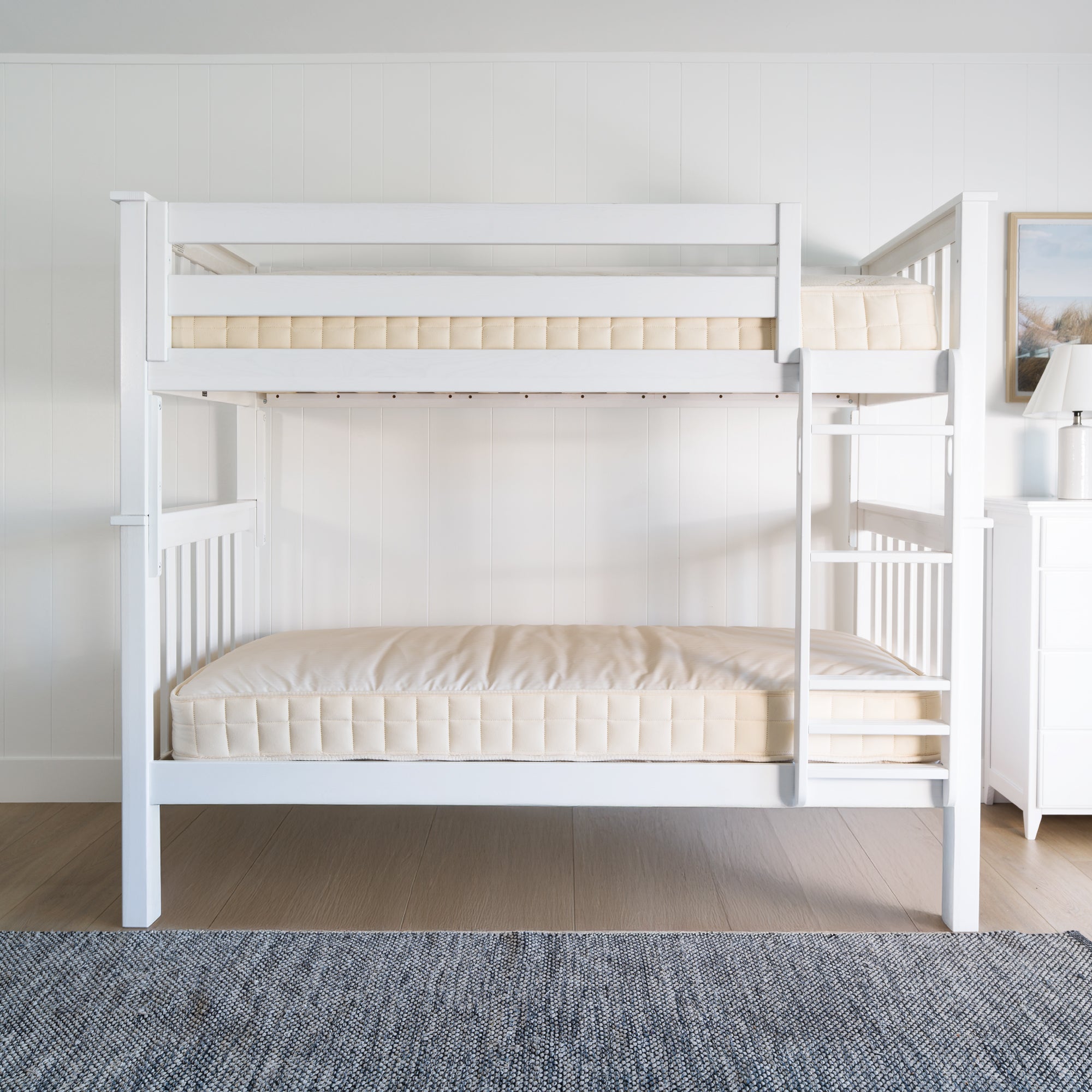 White wooden bunk bed with bare mattresses in a bright, minimalist bedroom setting. #color_washed white  #size_Twin/Twin Bunk 