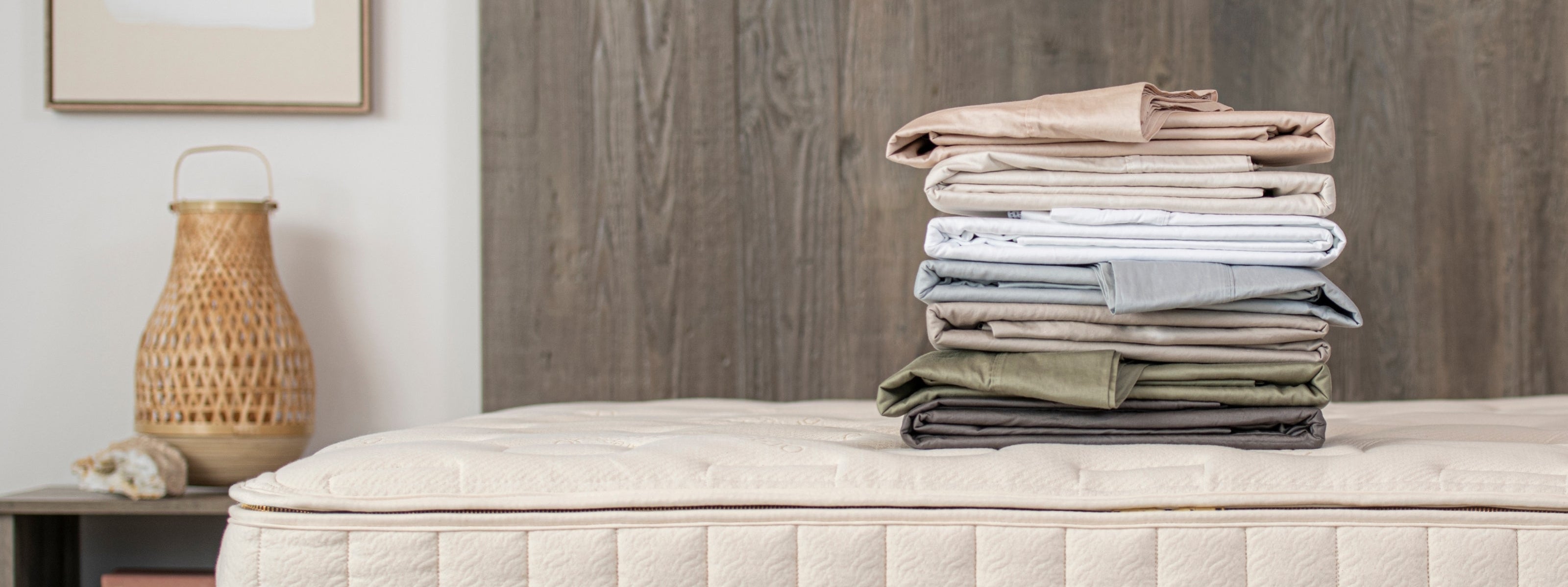Stack of folded bed sheets on a mattress with a wooden headboard and decorative items.
