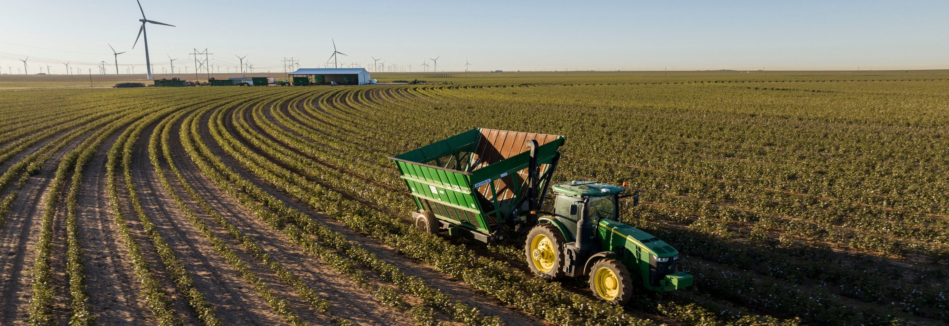 Tractor harvesting crops in a field with wind turbines in the background
