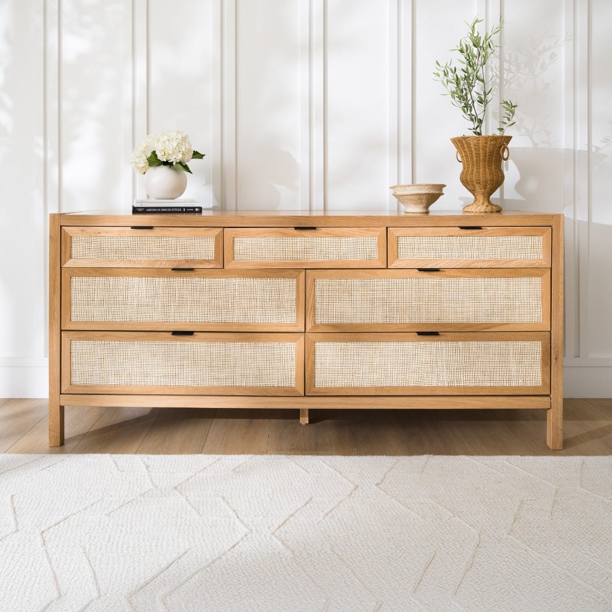 Wooden dresser with woven drawers in a room with light-colored walls and flooring.